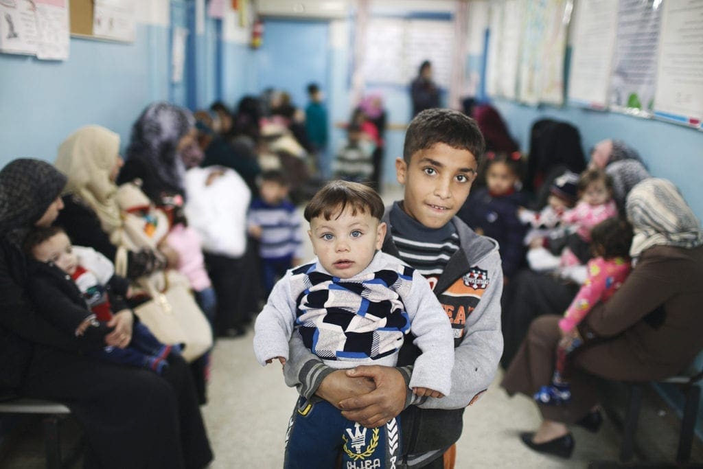 an adolescent holds a young boy in the waiting room of a clinic in Gaza.