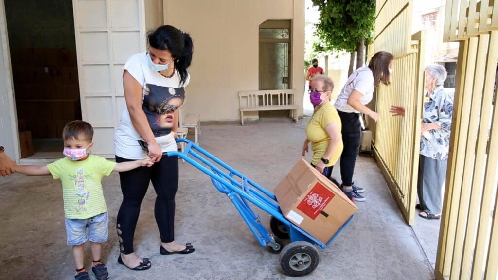 a masked woman and her child wheel a box on a cart.