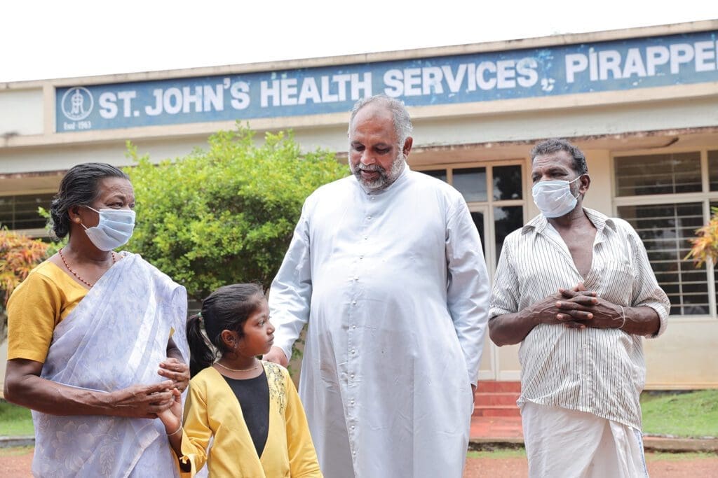 in Kerala, India, a priest chats outside with two grandparents and their granddaughter.