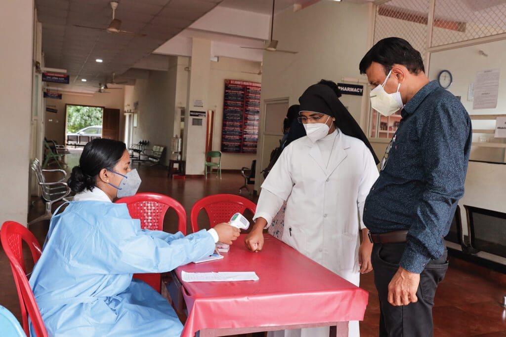 a hospital worker in southern India takes the temperature of two visitors during the pandemic.