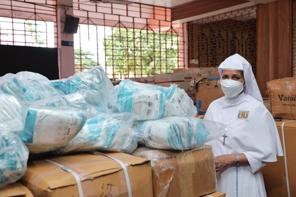 a nun stands near stacks of supplies as tall as she is.