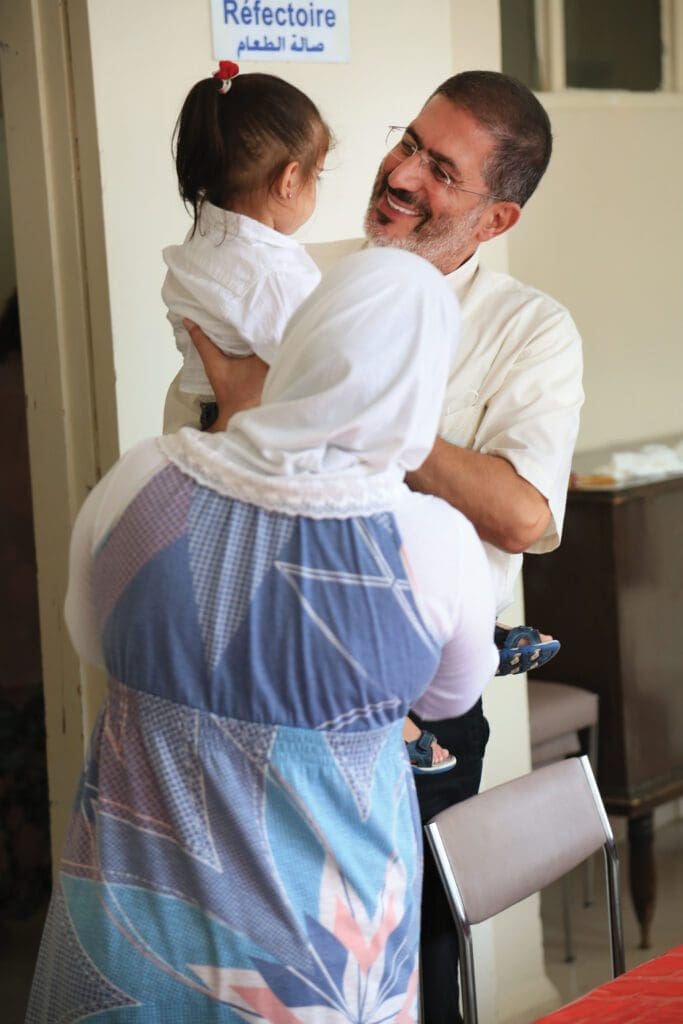 a man holds a child while her mother stands beside.