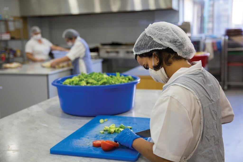 a young woman in gloves, a mask and a hair net chops vegetables at message de paix.
