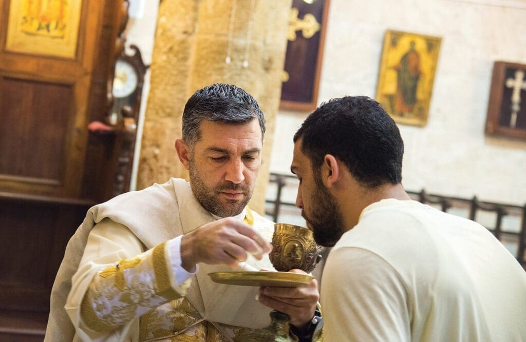 a priest gives communion to a young man during the Divine Liturgy.