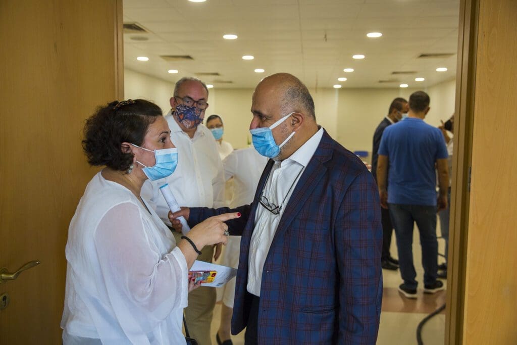 men and women wearing masks chat at the entrance of a large room.