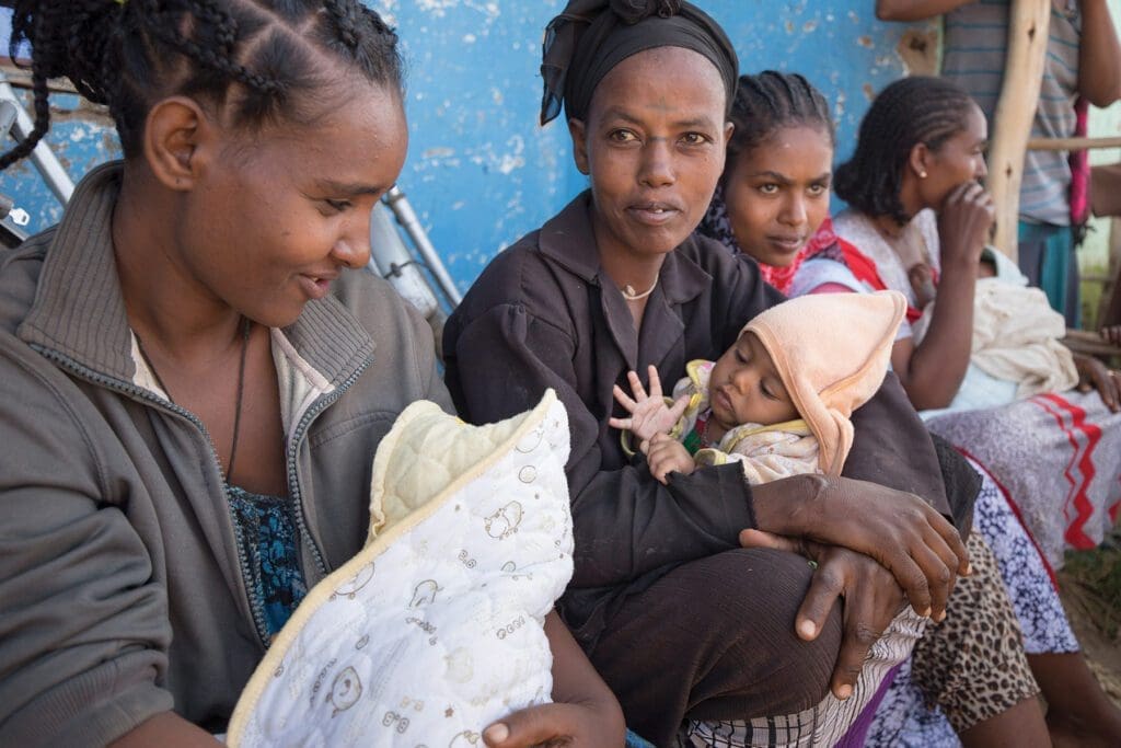 four young mothers sit cradling their infants by the side of a building.