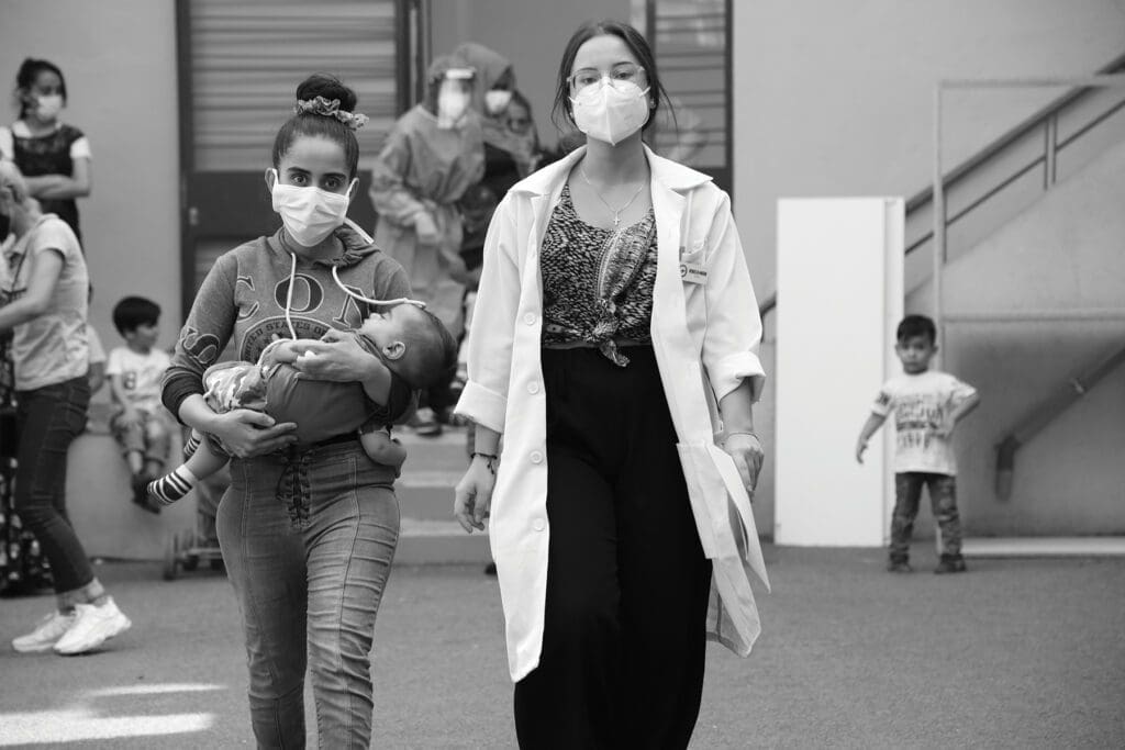 a health care worker walks beside a mother carrying her child.