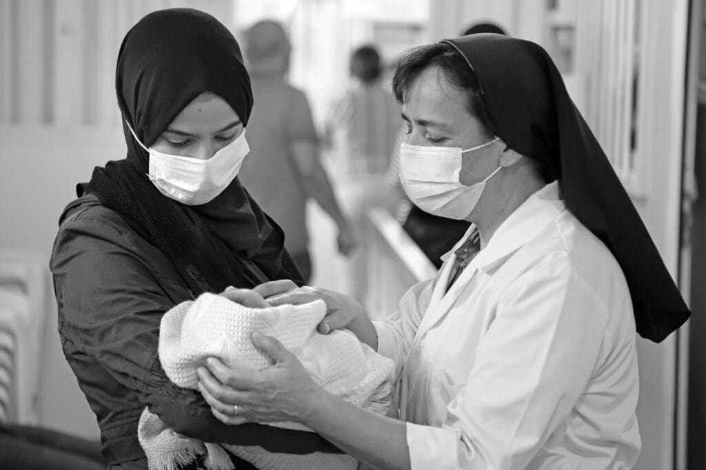 a nun inspects an infant held by a young woman.