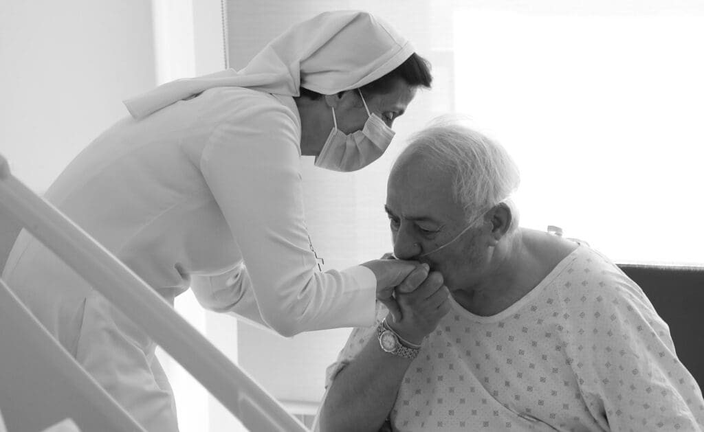 an elder patient in lebanon kisses the hand of a nun providing health care.
