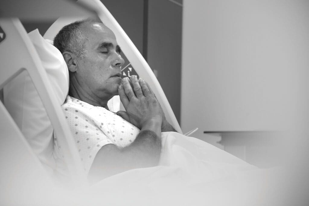 lebanese man in a hospital bed with eyes closed and hands folded.