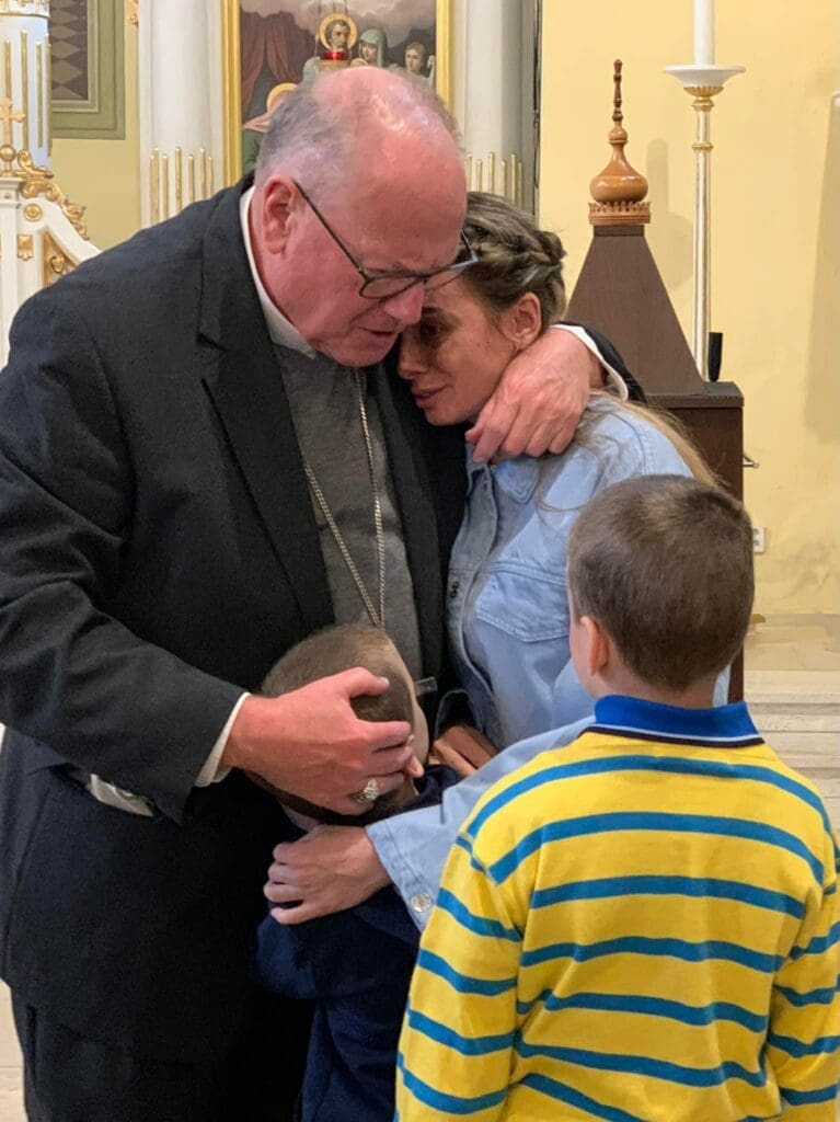 Cardinal Timothy Dolan comforts a Ukrainian woman and her children who fled Ukraine to Kosice, Slovakia. The woman shared her testimony during a vespers service at the Greek Catholic cathedral in Kosice on 30 April.