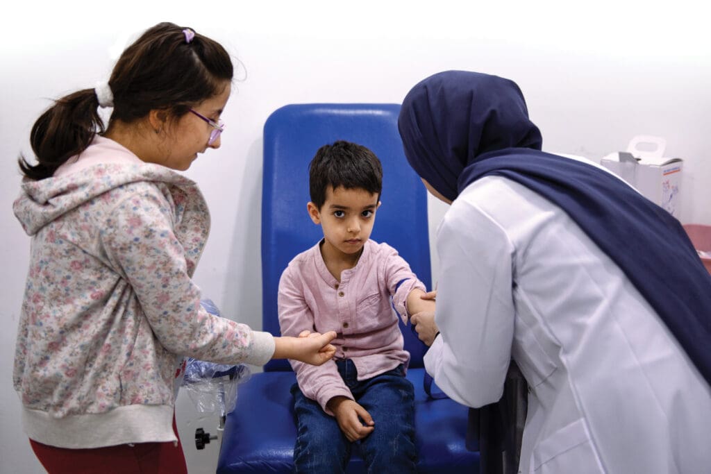 Matias Atran Bahjat, 6, prepares to have his blood drawn at the dispensary. His older sister (left) lends him support.