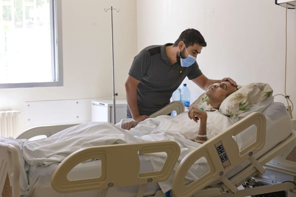A man consoles another man, a patient suffering acute rheumatism at Bhannes hospital.