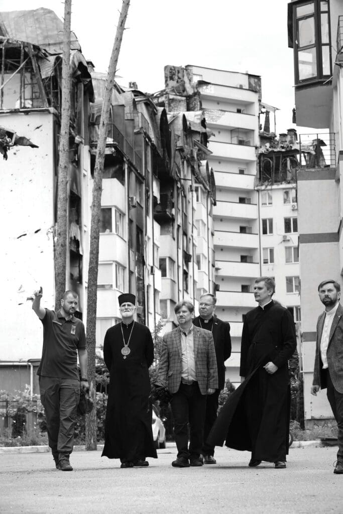 Archbishop Gudziak walks in a destroyed Ukrainian neighborhood with five other men.