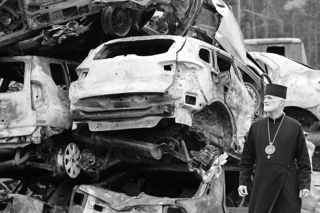 Archbishop Borys Gudziak walks amongst burnt cars in Bucha