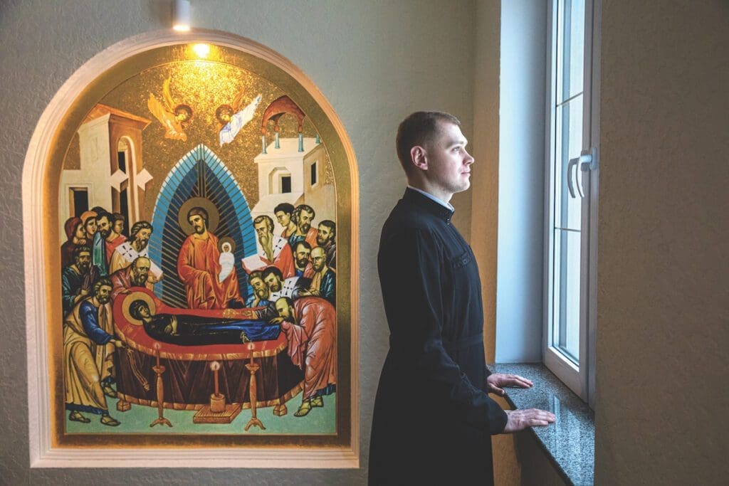 A seminarian looks out the window, an icon is to his left