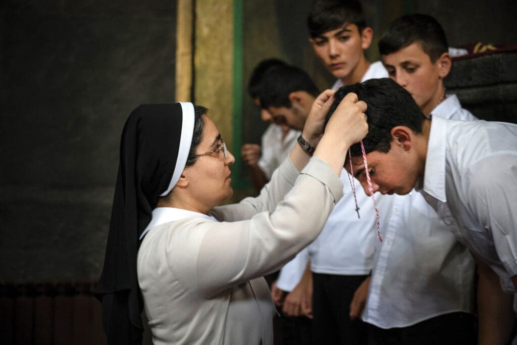 A religious sister puts a cross on a youth while other youths observe.