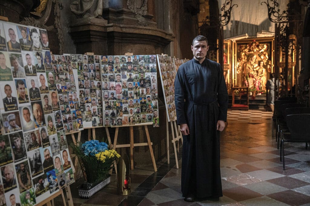 Father Andriy Khomyshyn stands next to photos of Ukrainian soldiers who died in the war against Russia.